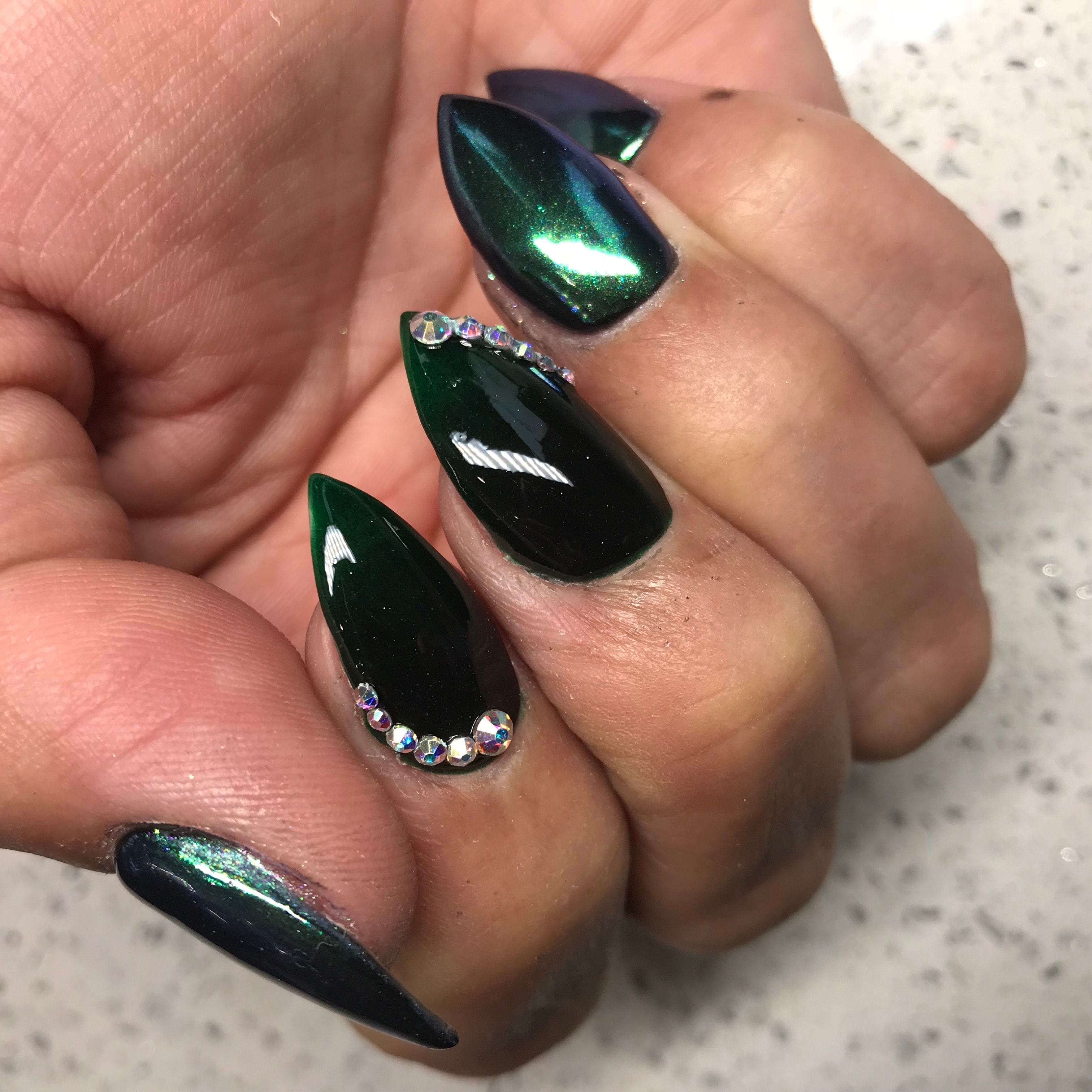 Deep green chrome nails with rhinestone embellishments